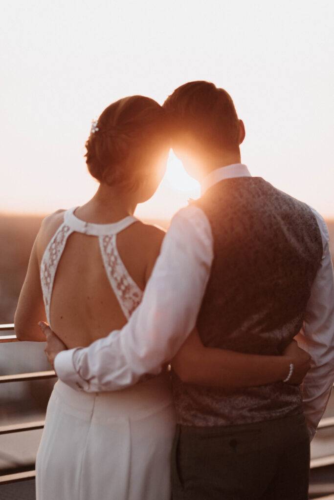 Das Brautpaar ist von hinten zu sehen, wie sie Richtung Sonnenuntergang schauen. Hochzeitsfotograf-Hamburg