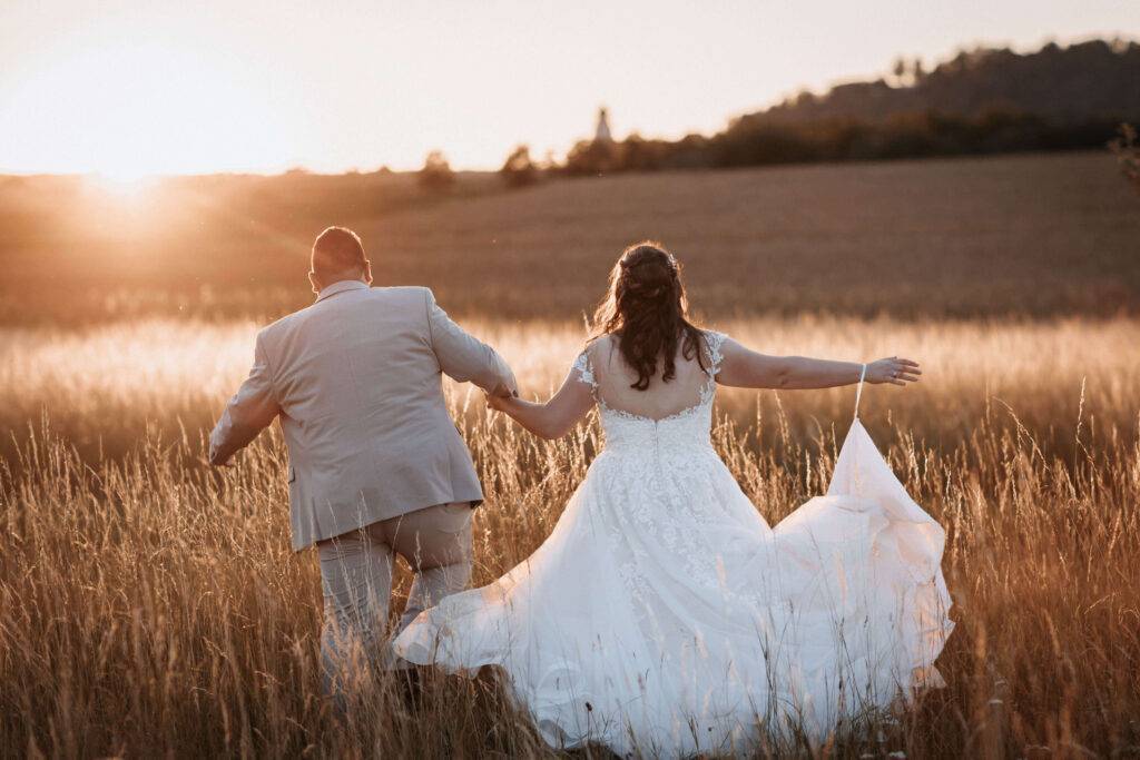 Golden Hour - Das Hochzeitspaar läuft Hand in Hand durch ein Kornfeld