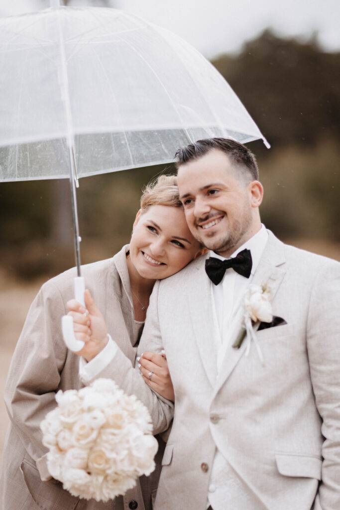 Das Brautpaar steht unter einem Transparenten Regenschirm und schaut dabei in die Kamera. Hochzeitsfotograf-Hamburg