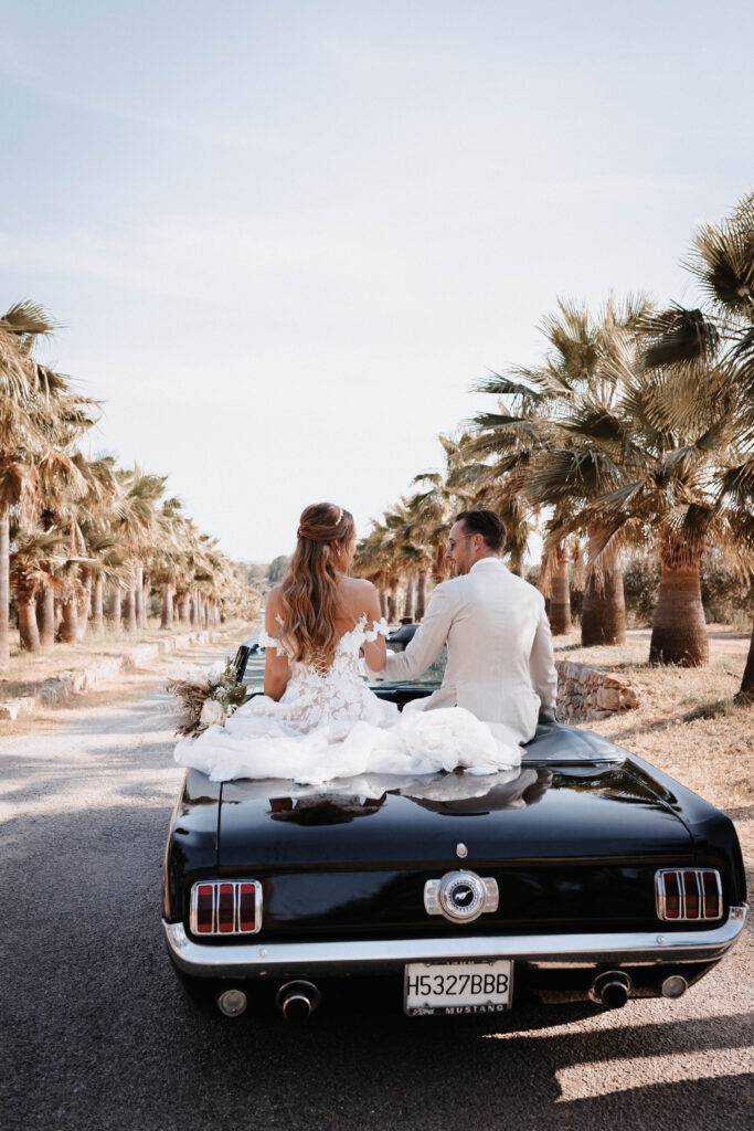 Das Brautpaar sitzt auf einem Mustang Carpio hinten drauf und fahren durch eine alle von Palmen von Mallorca. Hochzeitsfotograf-Hamburg