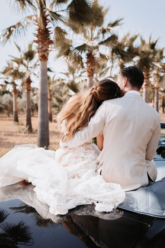 Das Brautpaar sitzt auf einem Mustang Carpio hinten drauf und fahren durch eine alle von Palmen von Mallorca. Hochzeitsfotograf-Hamburg