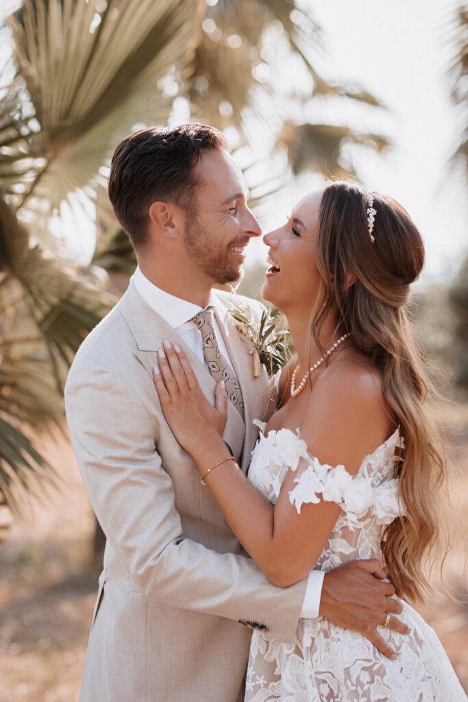 Das Brautpaar steht in einer Allee von Palmen hintereinander und schauen sich dabei an. Hinter ihnen steht ein Mustang mit Blumen beschmückt. Hochzeitsfotograf-Hamburg