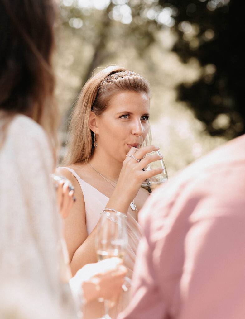 Aufnahme von einem Gast, welcher grad aus einem Glas durch ein Strohhalm trinkt. Sie ist Blond und um vordergrund sind Menschen zu sehen
