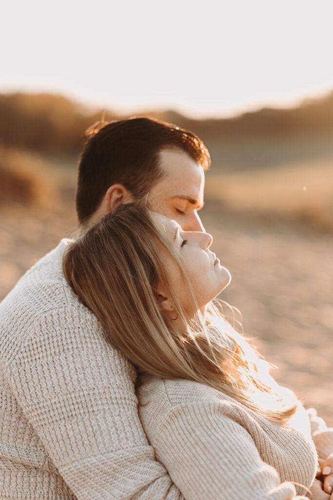 Bei Sonnenuntergang sitzt das Brautpaar mit geschlossenen Augen in den Dünen. Hochzeitsfotograf Hamburg. Hochzeitsfilm Hamburg