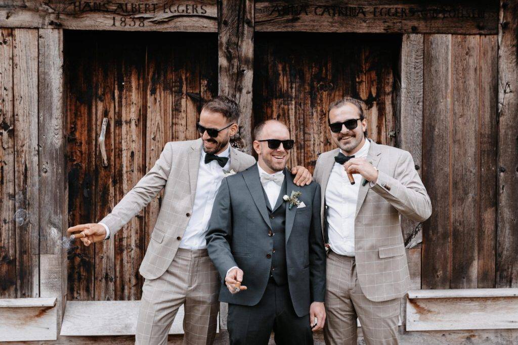 Gruppenaufnahme von dem Bräutigam und seinen Freunden. Sie sind zu dritt und der Bräutigam steht in der Mitte. Alle drei haben eine Zigarre in der Hand und eine Sonnenbrille auf. Hochzeitsfotograf-hamburg