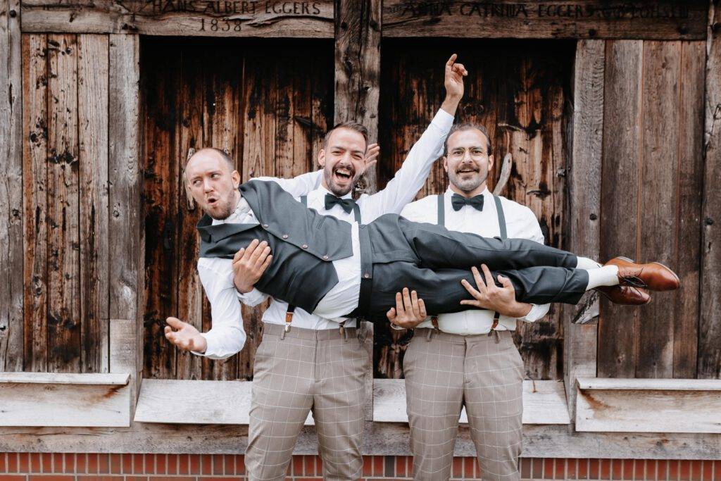 Der Bräutigam wird von zwei Freunden längs hochgehalten. Alle geben dabei einen Arm in die Höhe. Hochzeitsfotograf-hamburg