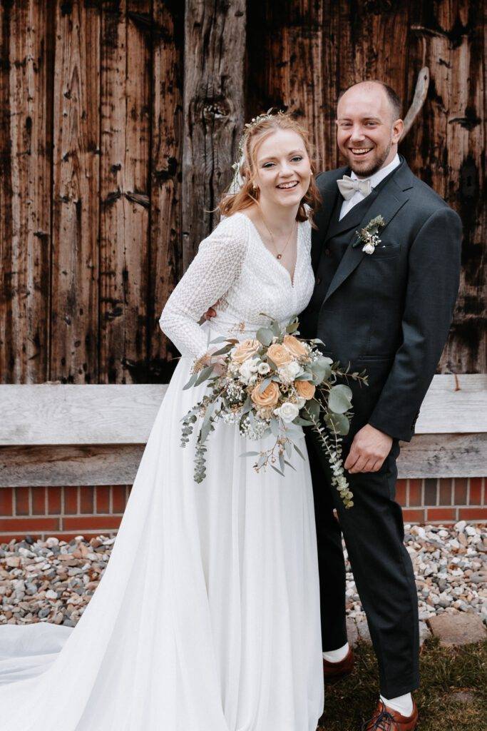 Das Brautpaar steht lachend voreinander und schaut dabei in die Kamera. Die Braut hält dabei Ihren Brautstrauß in der rechten Hand. Hochzeitsfotograf-hamburg