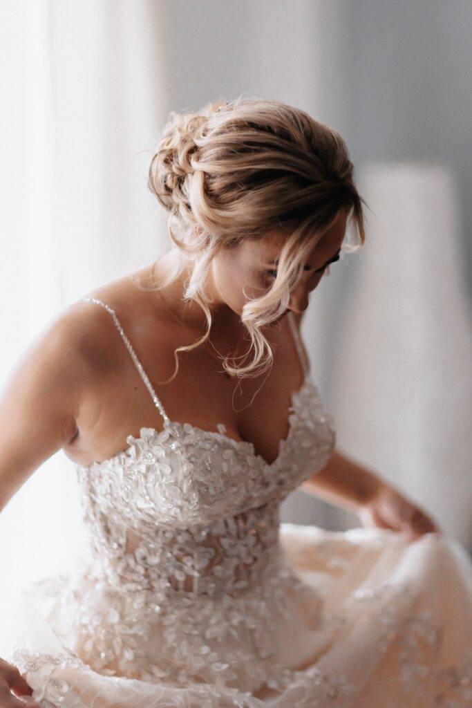 Nahaufnahme von einer Braut beim Getting Ready. Sie hat ein weißes Glitzerkleid an und schaut mit Ihren lockigen Haar auf den Boden