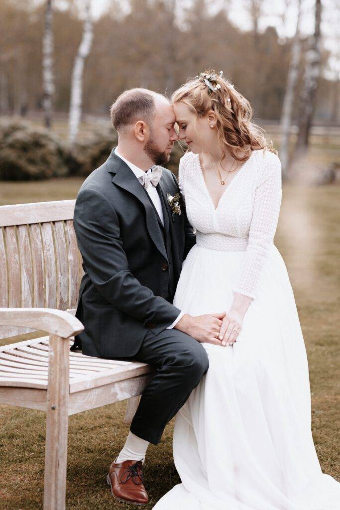 Der Bräutigam sitzt auf einer Bank und die Braut auf seinem Bein. Beide haben Ihre Stirn an die Stirn des anderen gerichtet. Hochzeitsfotograf-hamburg