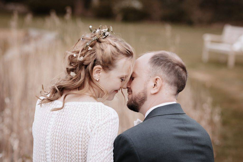 Der Bräutigam sitzt auf einer Bank und die Braut auf seinem Bein. Beide haben Ihre Stirn an die Stirn des anderen gerichtet. Hochzeitsfotograf-hamburg