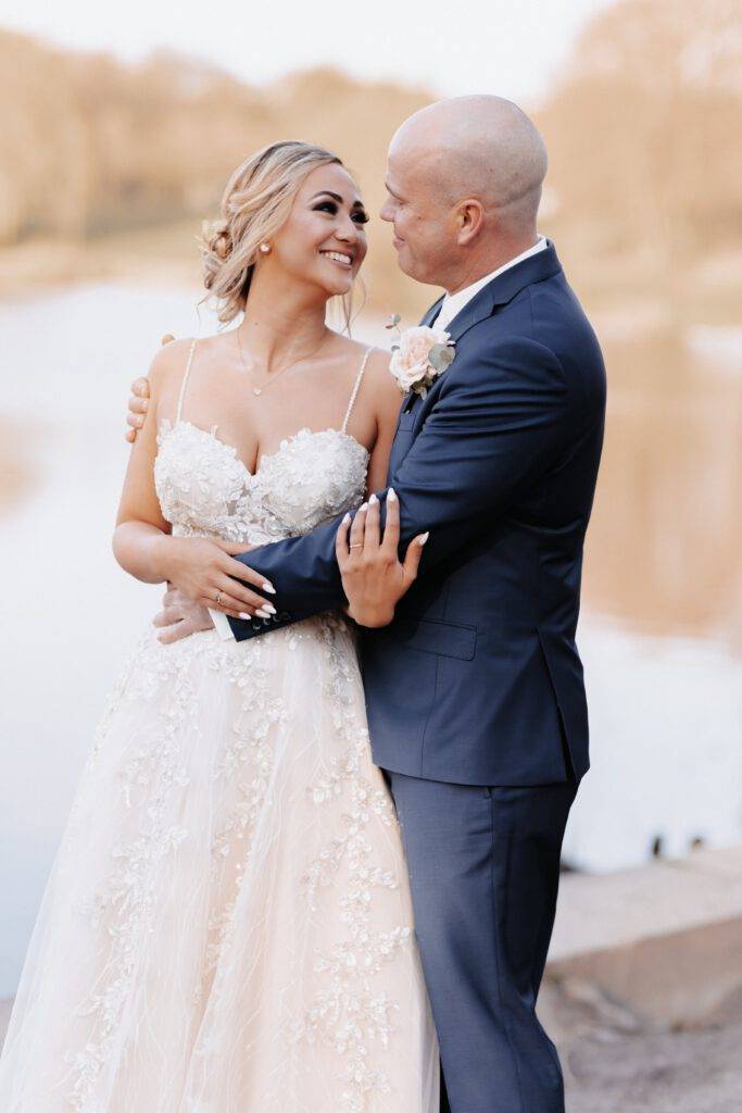 Das Brautpaar schaut sich in die Augen und hat sich dabei im Arm. Der Bräitgam hat ein blauen Anzug an und die Braut ein trägerloses Kleid