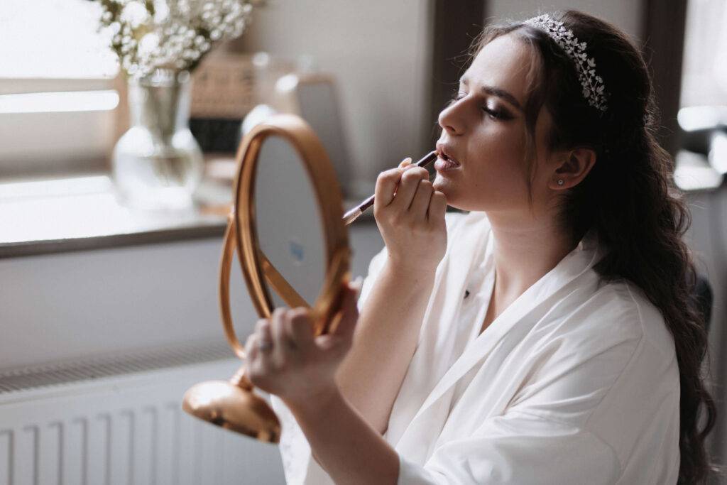 Ein junges Mädchen hält sich einen goldenen Spiegel vors Gesicht und zieht sich dabei die Lippen nach.