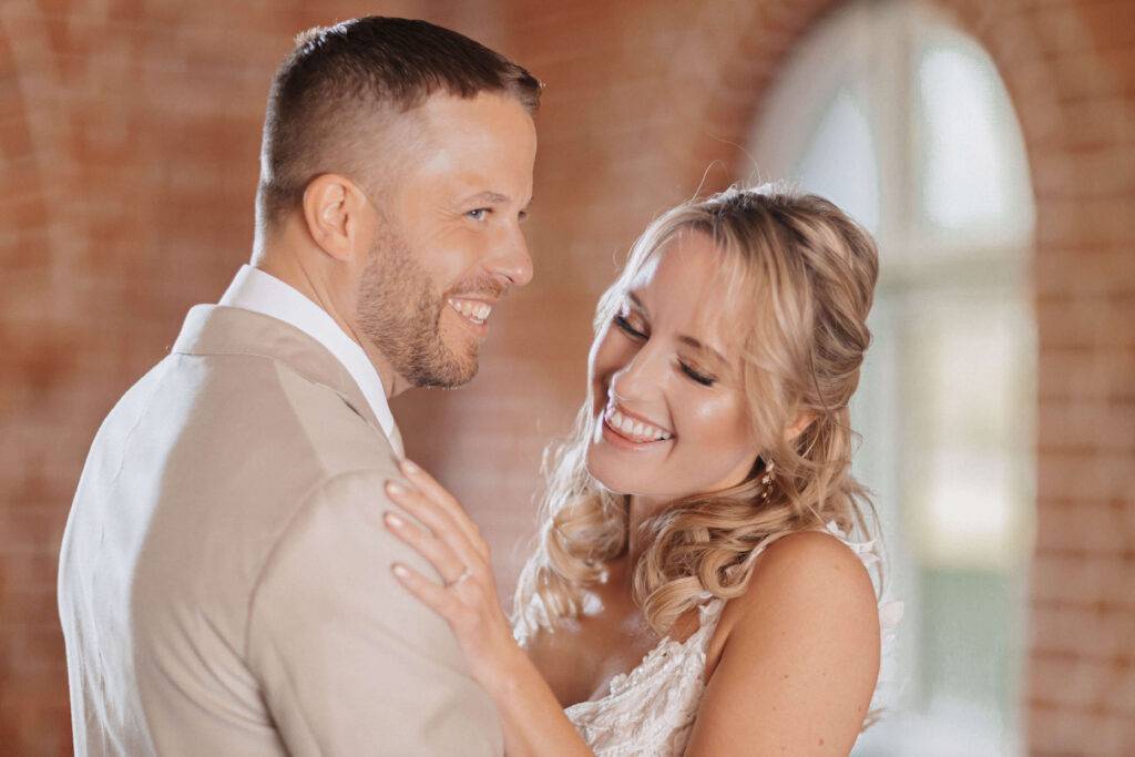 Man sieht eine Portait Aufnahme von einem jungen Pärchen, die sich anlachen. Dabei hält die blonde Frau ihre Hand auf seiner Schulter.