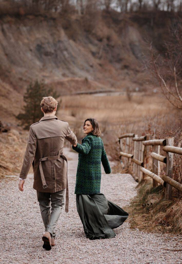 Das Brautpaar geht einen Weg. Es ist von hinten zu sehen. Die Braut geht ein stück weiter vor und schaut nach hinten zu Ihrem Bräutigam. Hochzeitsfotograf Hamburg. Hochzeitsfilm Hamburg