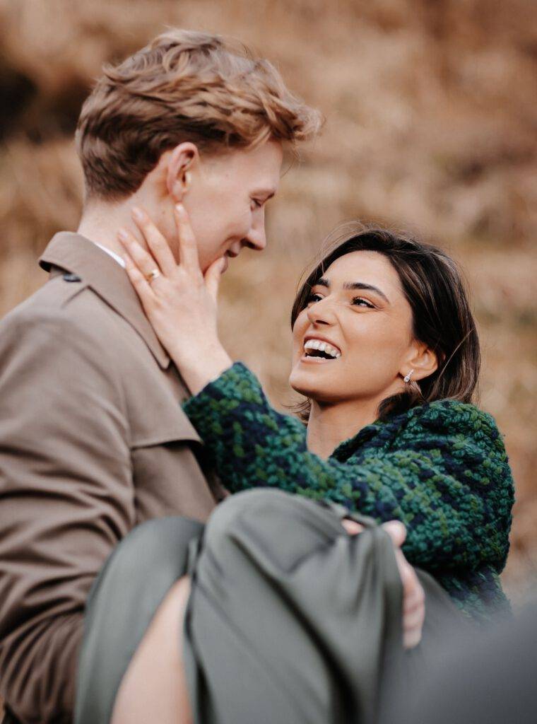 Der Bräutigam hat seine Braut auf dem Arm. Die Braut schaut den Bräutigam lachend an und hat ihre Hand an seiner Wange. Hochzeitsfotograf Hamburg. Hochzeitsfilm Hamburg