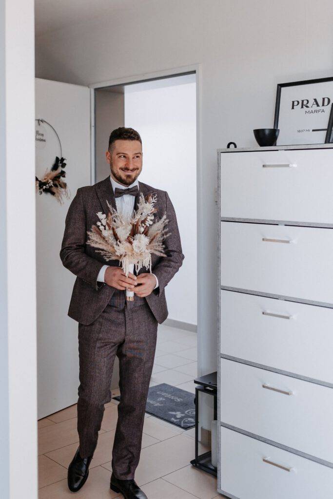 Der Brautpaar kommt zum Firstlook in die Wohnung mit dem Brautstrauß rein und schaut zu seiner Braut. Hochzeitsfotograf Hamburg. Hochzeitsfilm Hamburg