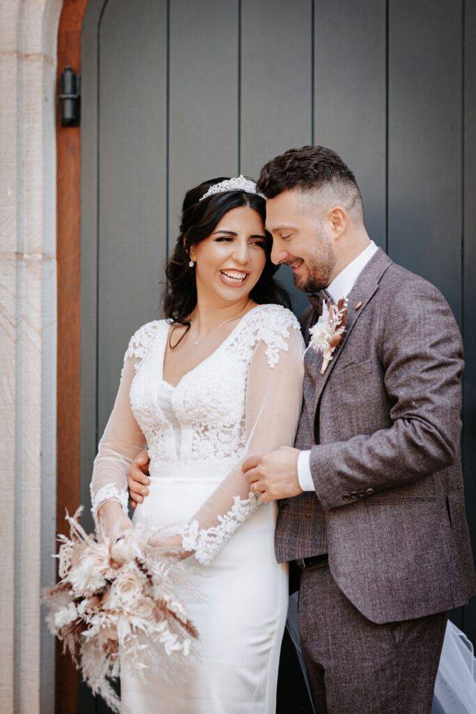 Vor einer Tür steht das Brautpaar und schaut sich lachend an. Hochzeitsfotograf Hamburg. Hochzeitsfilm Hamburg