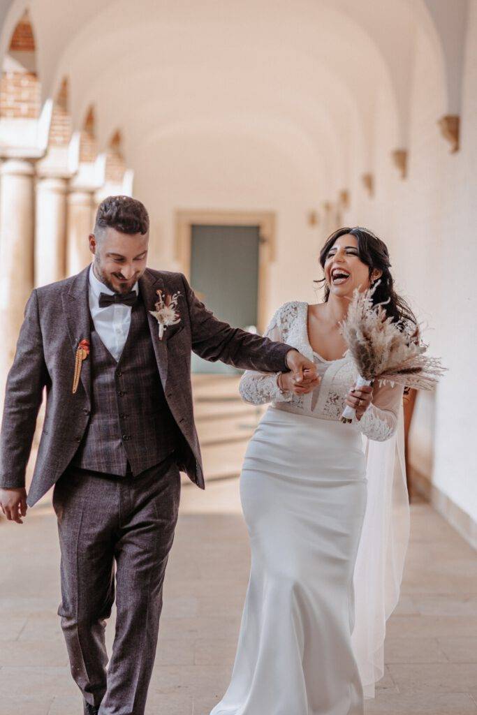 Lachend, Hand in Hand geht das Brautpaar den Weg entlang mit dem Gesicht zur Kamera Hochzeitsfotograf Hamburg. Hochzeitsfilm Hamburg