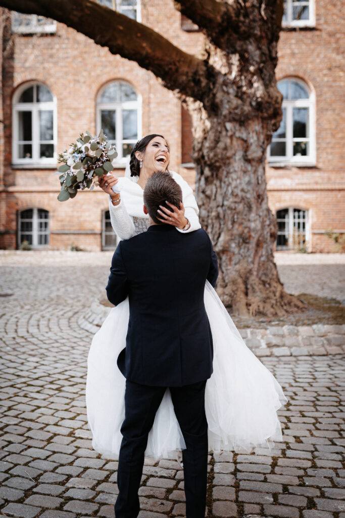 Das Hochzeitspaar tanzt vor einem Baum. Die Braut wird angehoben und lacht. Hochzeitsfotograf Hamburg. Hochzeitsfilm Hamburg