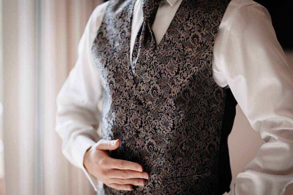 Detailaufnahme von der West des Bräutigams. Die Weste ist verschnörkelt. Braut und Bräutigam vor dem Pastor bei der Trauung. Hochzeitsfotograf Hamburg. Hochzeitsfilm Hamburg