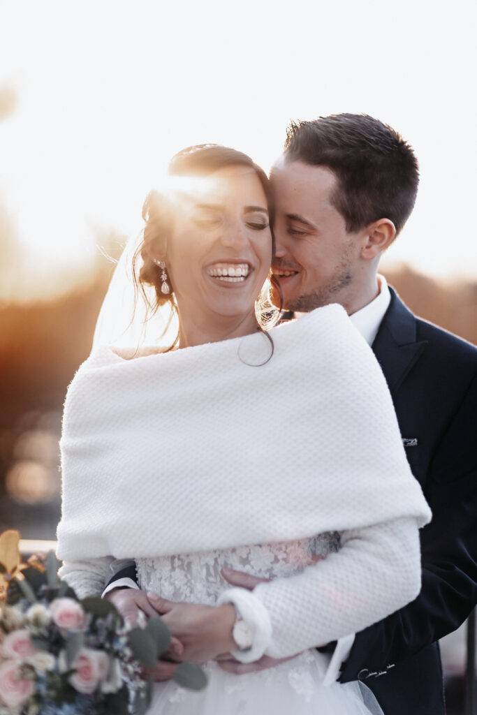 Das Brautpaar steht hintereinander bei Sonnenuntergang und lacht. Hochzeitsfotograf Hamburg. Hochzeitsfilm Hamburg